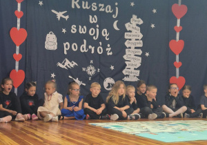 Jabłuszka siedzą po turecku na scenie w tle dekoracja