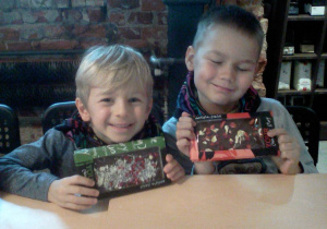 Dwóch chłopców przy stoliku pokazuje wykonane przez siebie czekolady