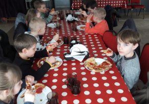 Dzieci siedza przy stoliku jedzą pizzę własnej roboty