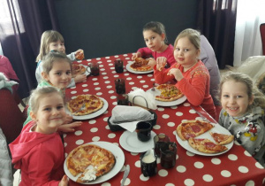 Dziewczynki siedzą przy stole, każda z nich je mini pizzę własnej roboty