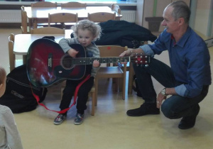 Chłopiec gra na gitarze obok kuza przy nim Pan prowadzący warsztaty