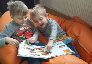 Chłopcy na pomarańczowym worku-pufie oglądają książkę