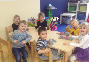 Dzieci siedzą przy stolikach, maja przed sobą wykonane zające wielkanocne